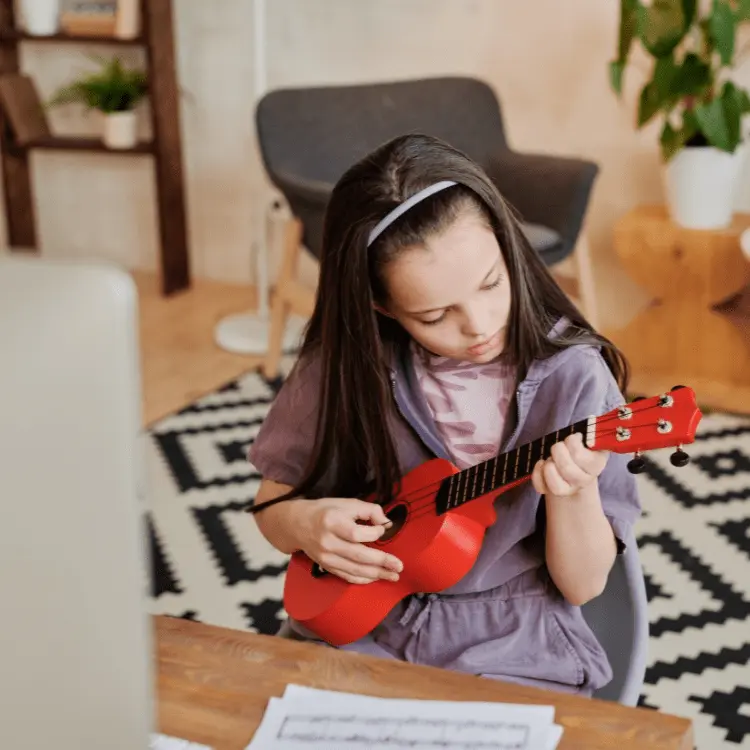 Enfant qui apprend à jouer du Ukulele en regardant un cours vidéo sur ordinateur